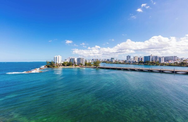 A coastal cityscape with a clear view of the ocean, a bridge, and a row of buildings along the shore. - Ocean Breeze Villa (San Juan)