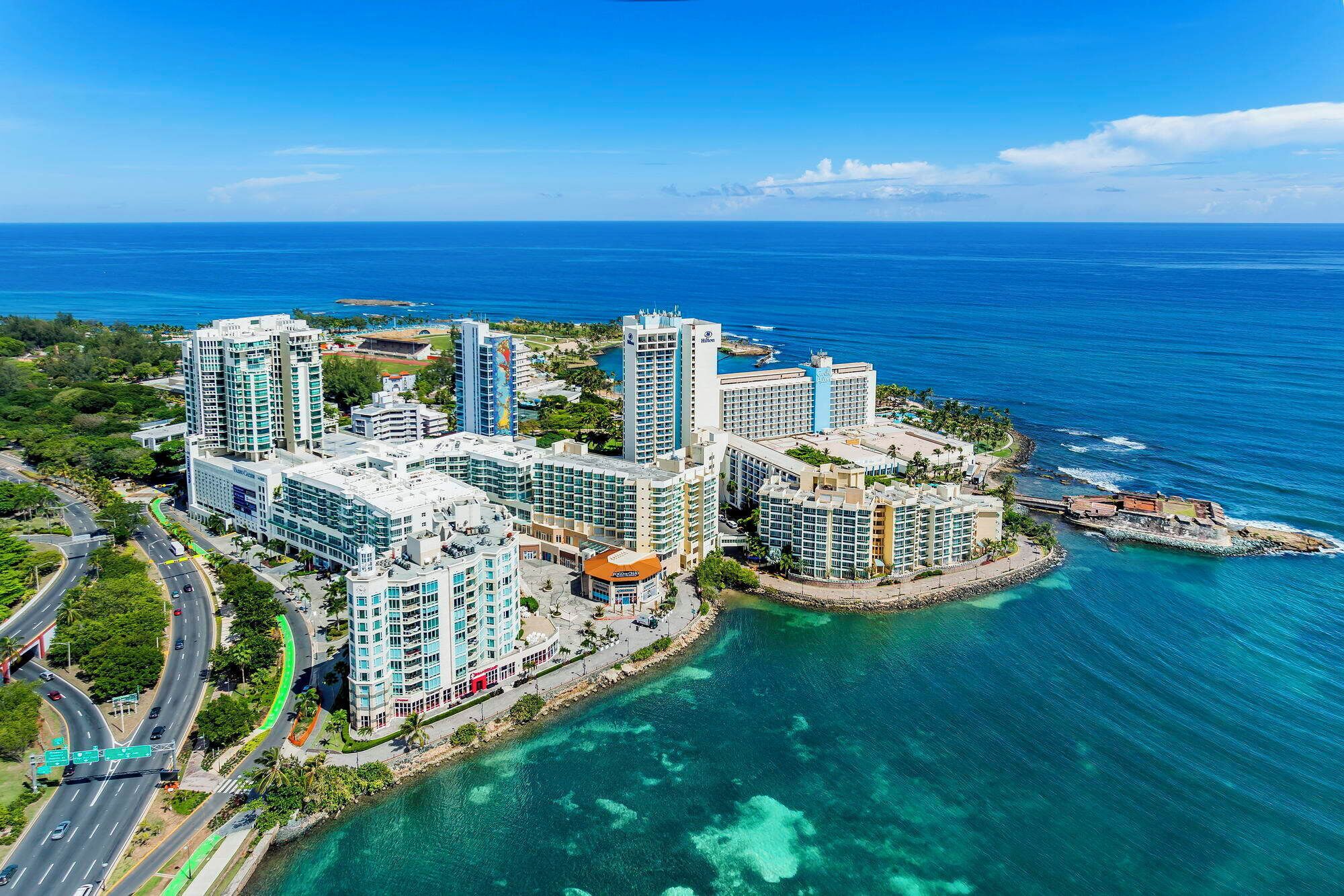 Un complejo hotelero frente al mar con varias torres, un puerto deportivo y aguas azul turquesa.