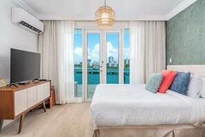 A hotel room with a large bed, a TV, a wardrobe, and a view of a cityscape through a glass door. - Ocean Breeze Villa (San Juan)