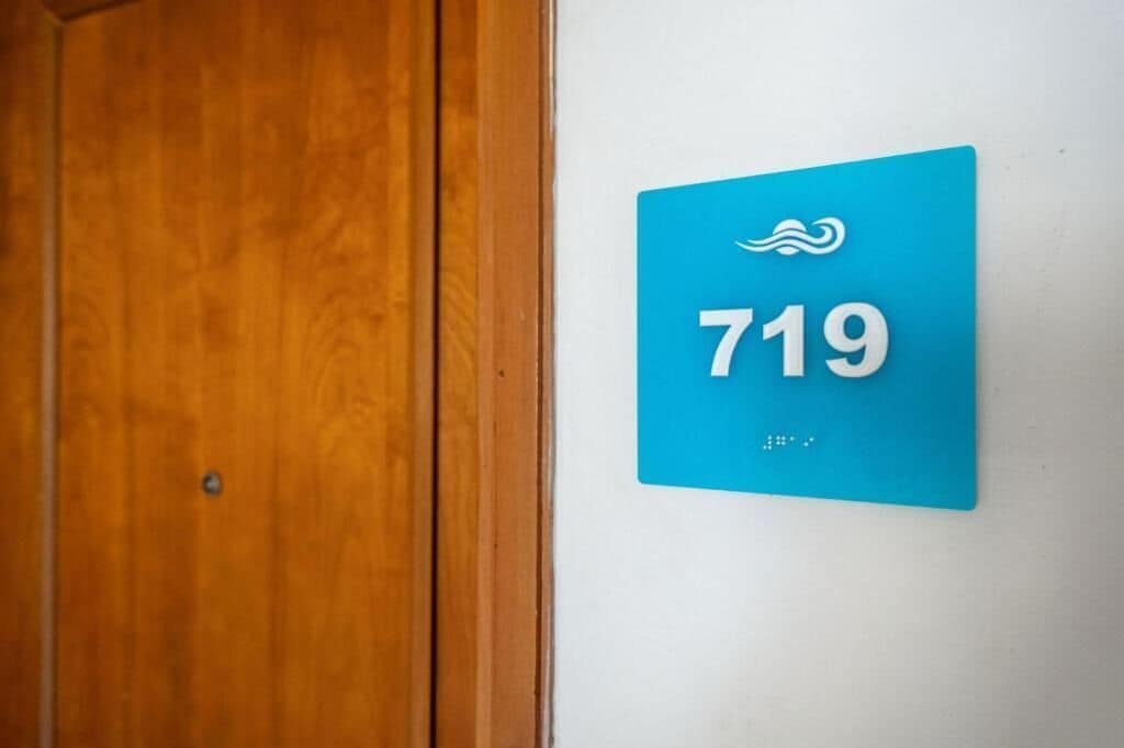 A blue sign with the number 719 on a white wall, next to a wooden door.