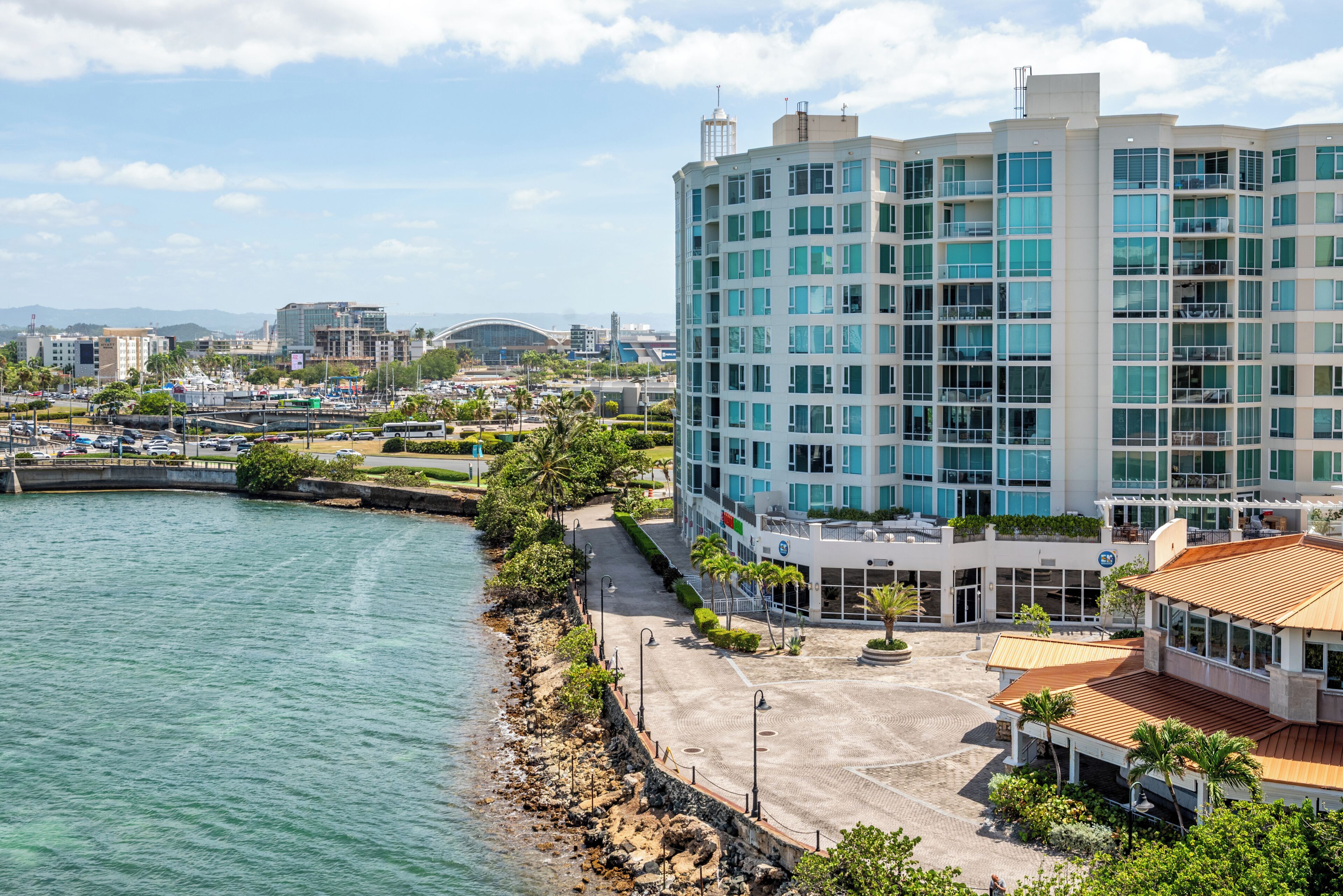 A coastal hotel with a view of the sea, a parking area, and a landscaped promenade.