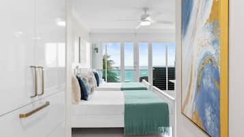 A bedroom with a bed, a view of the ocean, a ceiling fan, and a painting on the wall.