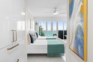 Un dormitorio con cama, vista al océano, ventilador de techo y un cuadro en la pared.