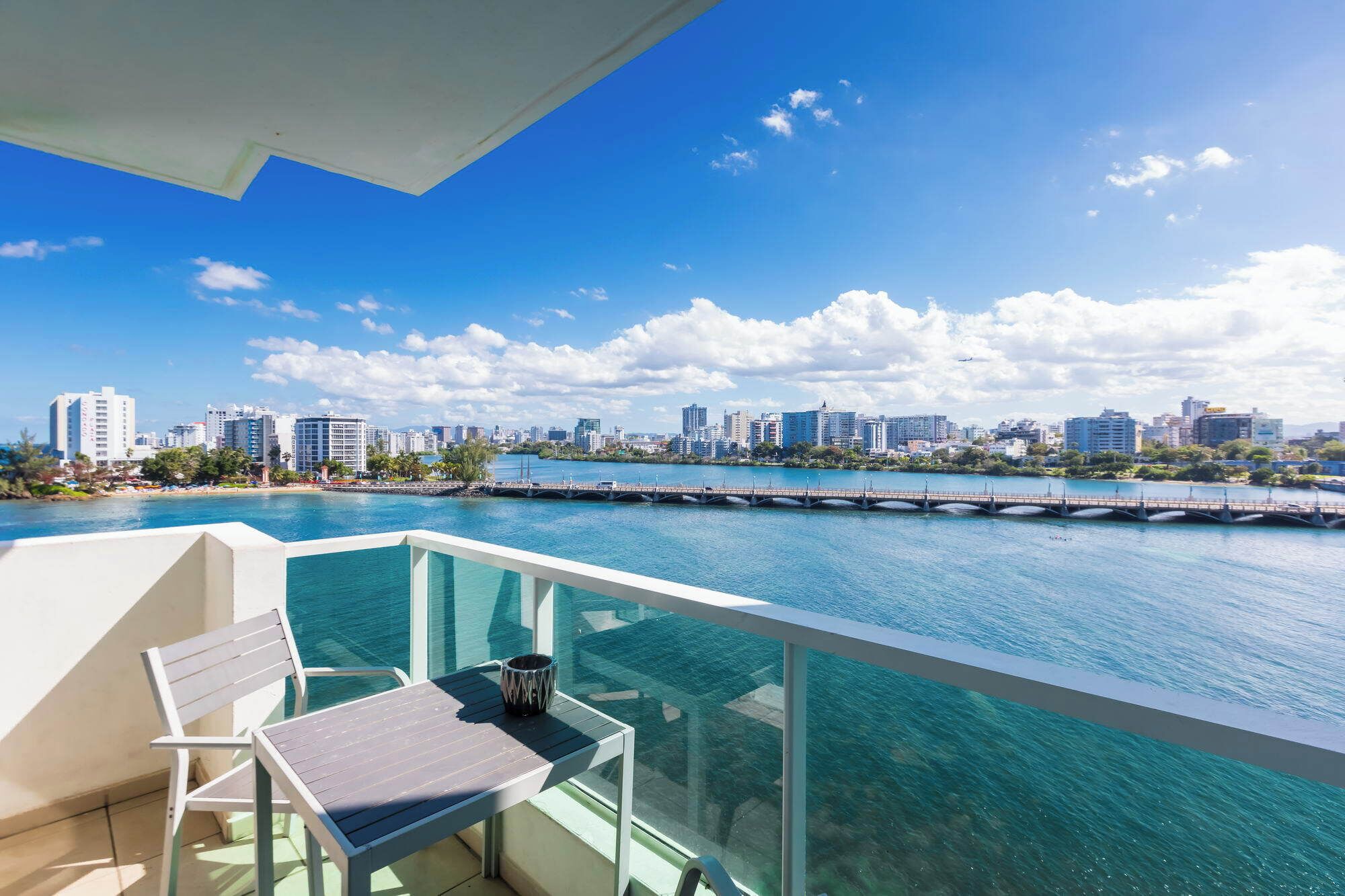 A balcony with a table and chairs overlooking a cityscape and a body of water.