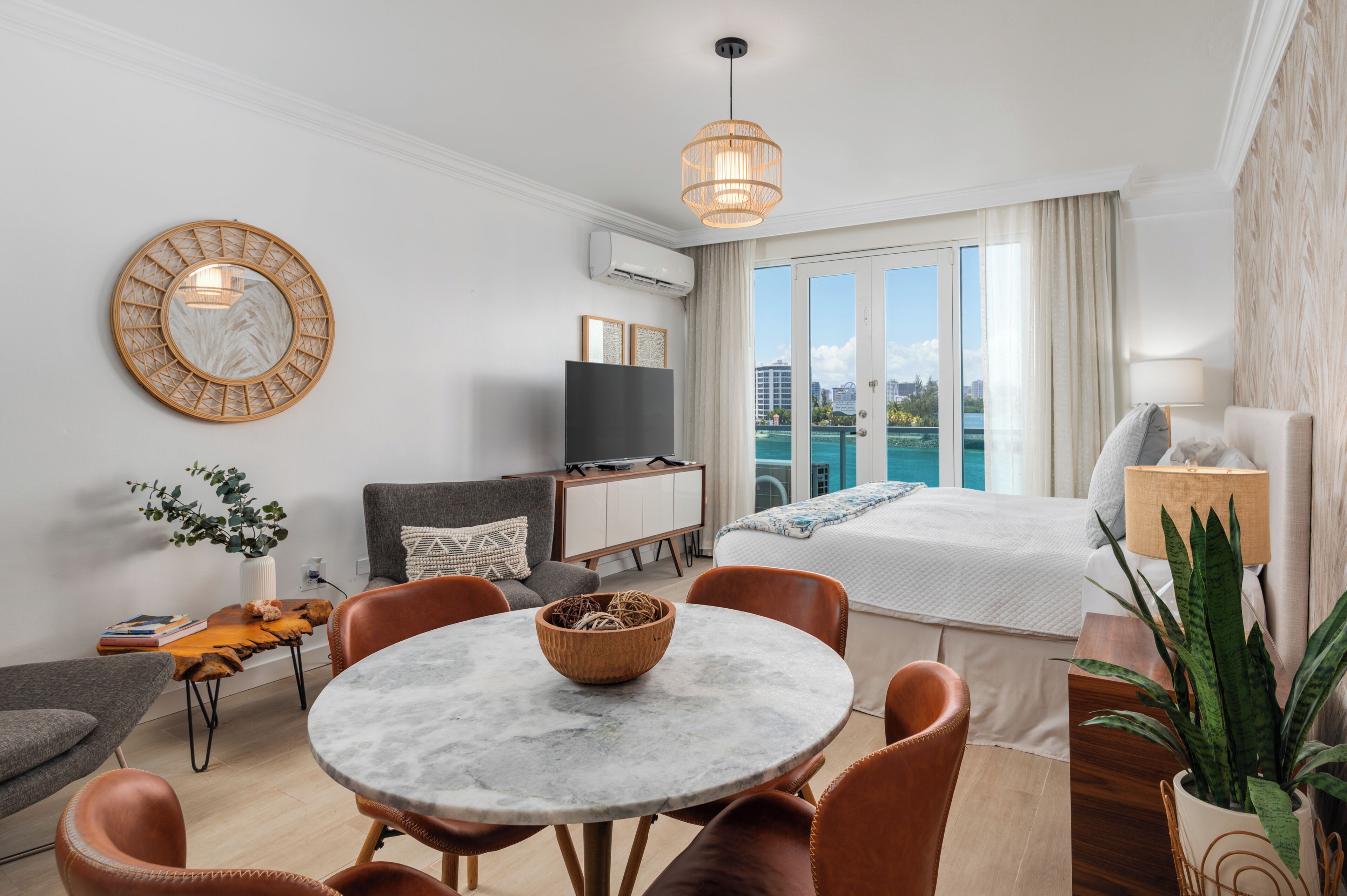 Ein modernes Hotelzimmer mit einem großen Bett, einem runden Esstisch und Blick auf die Stadt.