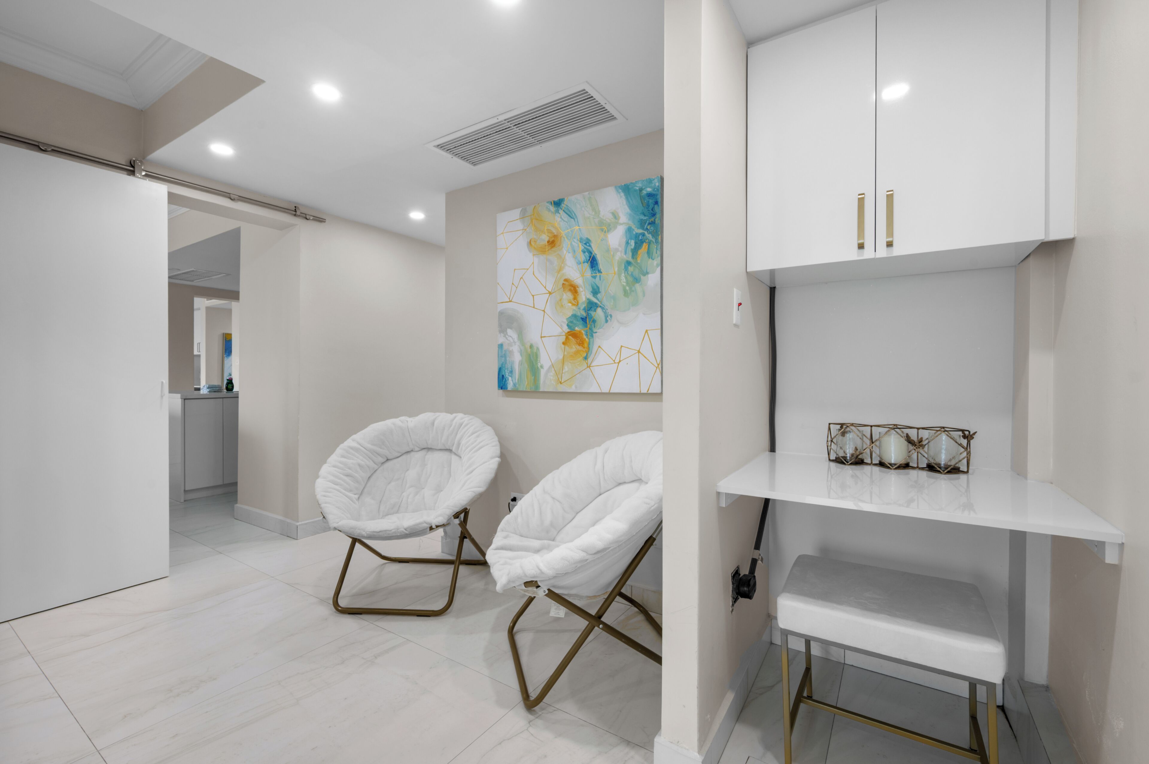Un intérieur moderne avec des murs blancs, un grand tableau abstrait et deux chaises blanches à cadre doré.
