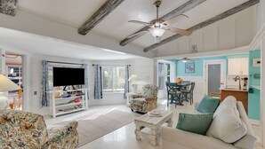 Un salon avec un téléviseur, un fauteuil à motifs floraux et un ventilateur de plafond.
