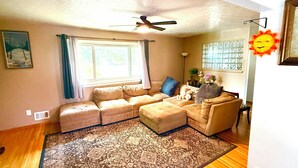 A living room with a sectional sofa, a small armchair, a floor lamp, and a large window with curtains. - Charming 2-bedroom + office house, safe, quiet, and convenient (Rochester)