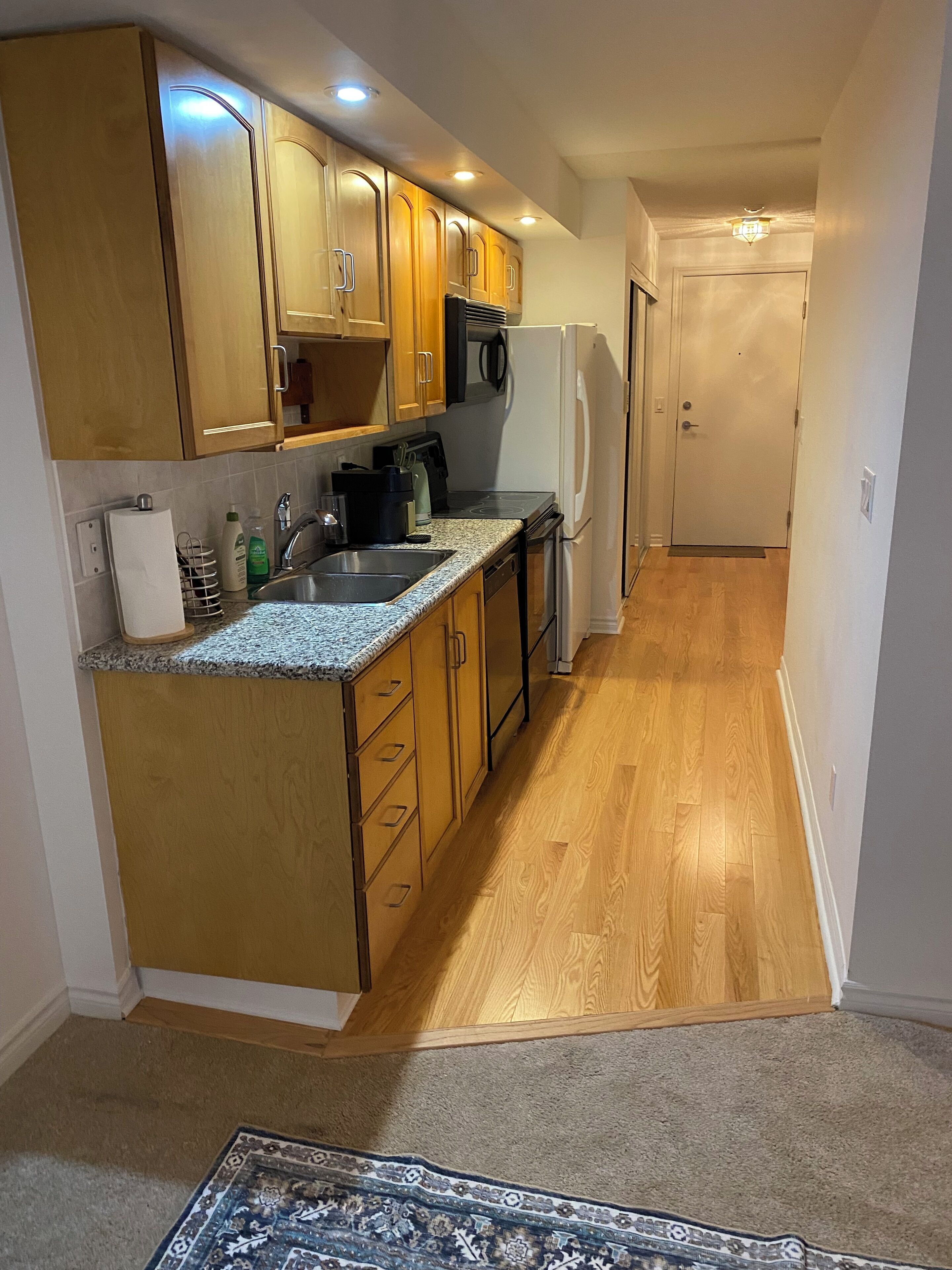 A compact kitchen with wooden cabinets, a granite countertop, a built-in microwave, and a refrigerator.