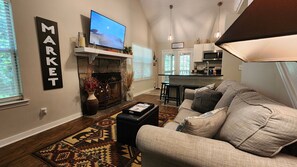 Living room featuring a sofa, stone fireplace, mounted TV, and an open kitchen view.