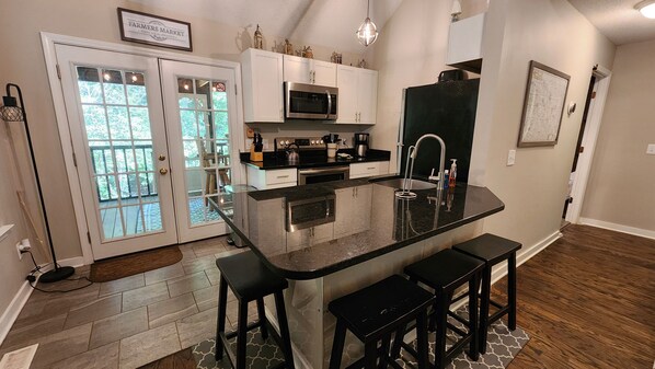 A kitchen with dark countertops, an island with barstools, and French doors.