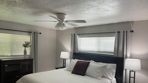 Ein Schlafzimmer mit einem Bett, zwei Nachttischen mit Lampen, einem Deckenventilator und einem Fenster mit Jalousien.