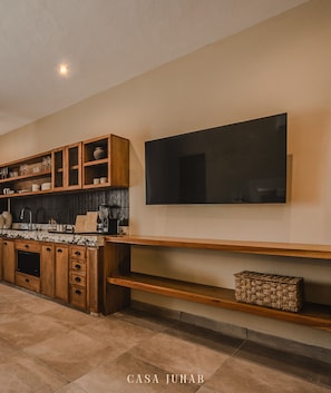 A modern kitchen with wooden cabinetry, a built-in stove, and a large flat-screen TV mounted on the wall.