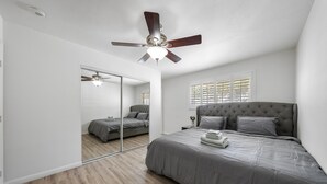 Un dormitorio con una cama grande, un ventilador de techo, un espejo y una ventana con persianas.
