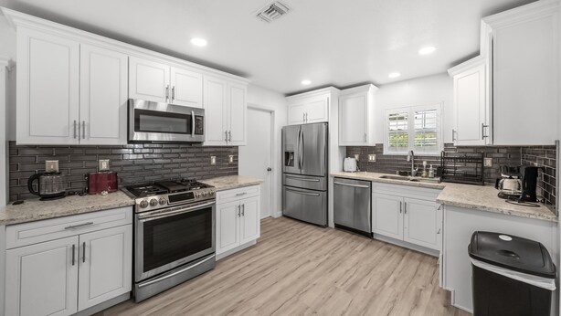 Una cocina moderna con gabinetes blancos, un refrigerador de acero inoxidable, un microondas, una estufa y una cafetera.