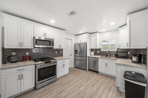 Una cocina moderna con gabinetes blancos, un refrigerador de acero inoxidable, un microondas, una estufa y una cafetera.