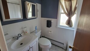 Ein Badezimmer mit weißem Waschbecken, Spiegel, Toilette und einem Fenster mit Vorhängen.