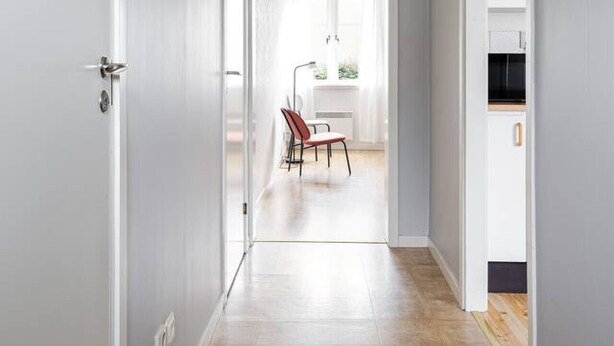 Un couloir avec une porte à gauche, une chaise au centre et un coin cuisine à droite.