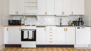 Une cuisine avec des meubles blancs, une cuisinière, un four à micro-ondes, un évier et une machine à café.