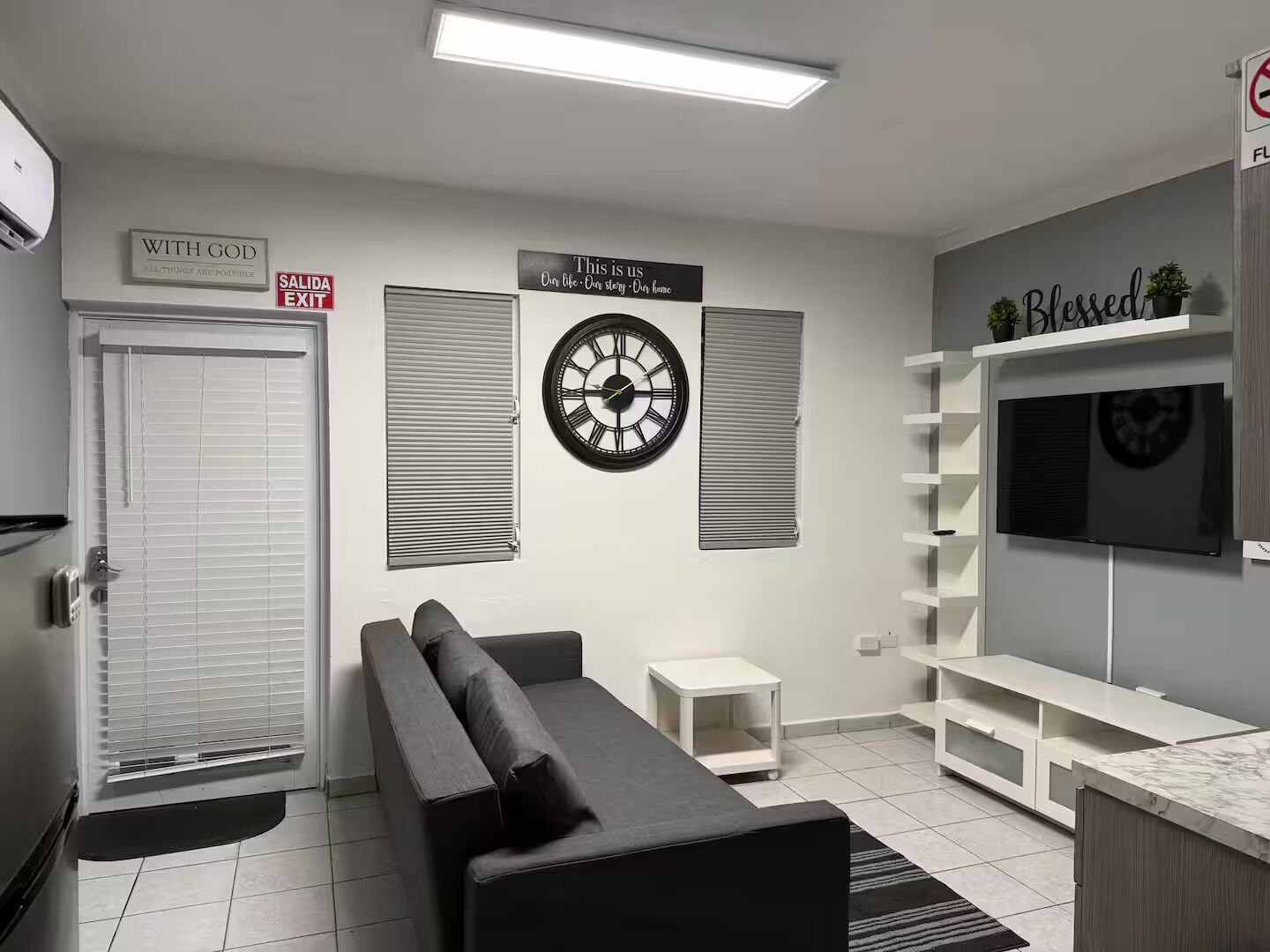 Una sala de estar moderna con un sofá, un reloj, un televisor y un cartel que dice 'CON DIOS TODO ES POSIBLE'.