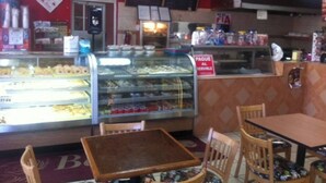 A bakery counter with a glass display case, a menu board, and a 'PAGUE AL SERVIR' sign. - Palmas View 2 (catano)