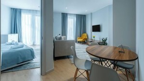 A modern hotel room with a bed, a sofa, a dining table, and a TV. - Mziuri Gardens Apartments (Makhinjauri)