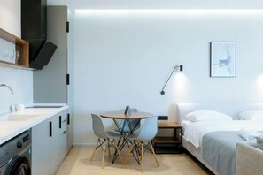 A modern hotel room with a kitchenette, a dining table with chairs, a bed, and a bedside table. - Mziuri Gardens Apartments (Makhinjauri)