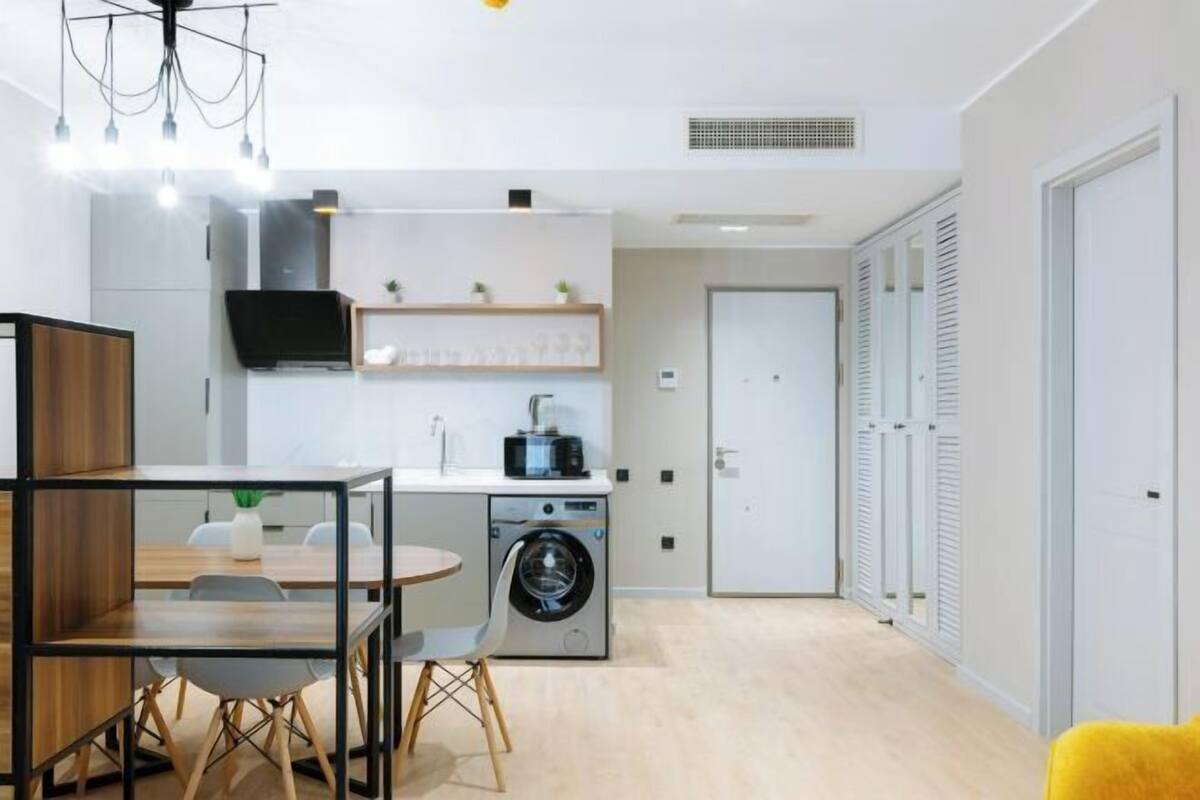Un espace de vie compact comprenant un coin repas, un lave-linge, un téléviseur et une porte dotée de volets à persiennes.