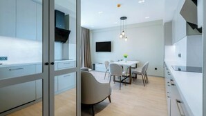 A modern kitchen with a dining area, a TV mounted on the wall, and a pendant light. - Mziuri Gardens Apartments (Makhinjauri)