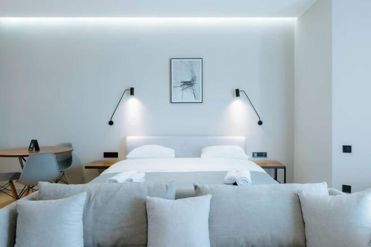 Une chambre d’hôtel moderne équipée d’un lit, de deux tables de chevet, d’un bureau, d’une chaise et d’une œuvre d’art accrochée au mur.