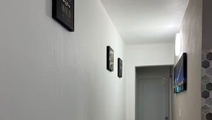 A narrow hallway with white walls and a speckled carpet. There are three framed signs on the wall, one of which reads "Always be Brave, Wild at Heart." The hallway leads to a door at the end.