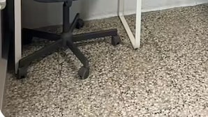 A room with a white air conditioner, a painting of a bullfighter, and a desk with a chair.