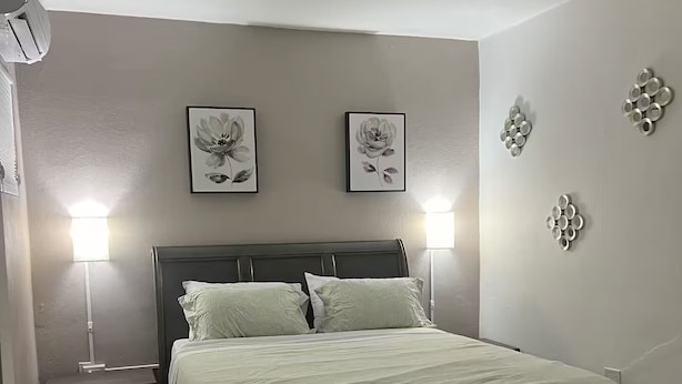 A bedroom with a dark wooden bed, two wall-mounted lamps, and two framed floral artworks.