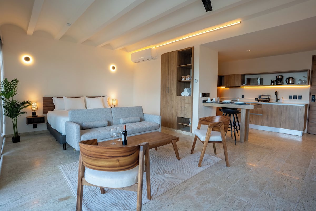Uma sala de estar moderna com sofá, mesa de centro e cadeiras. Há uma cozinha com mesa e cadeiras.