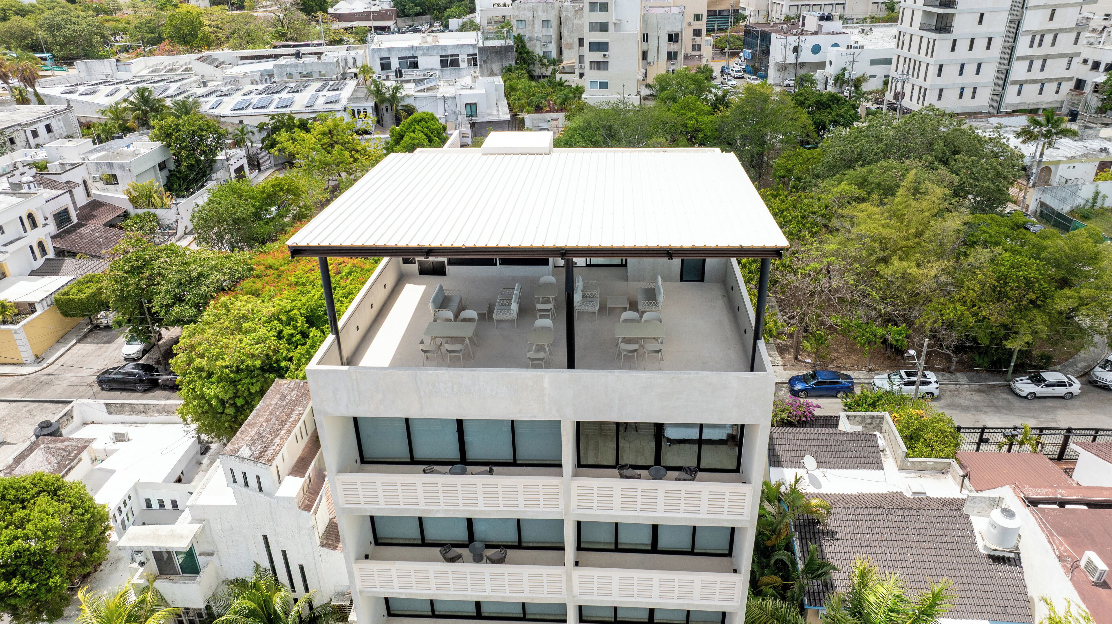 Ein mehrstöckiges Gebäude mit flachem Dach und einer Dachterrasse mit Außenmöbeln.
