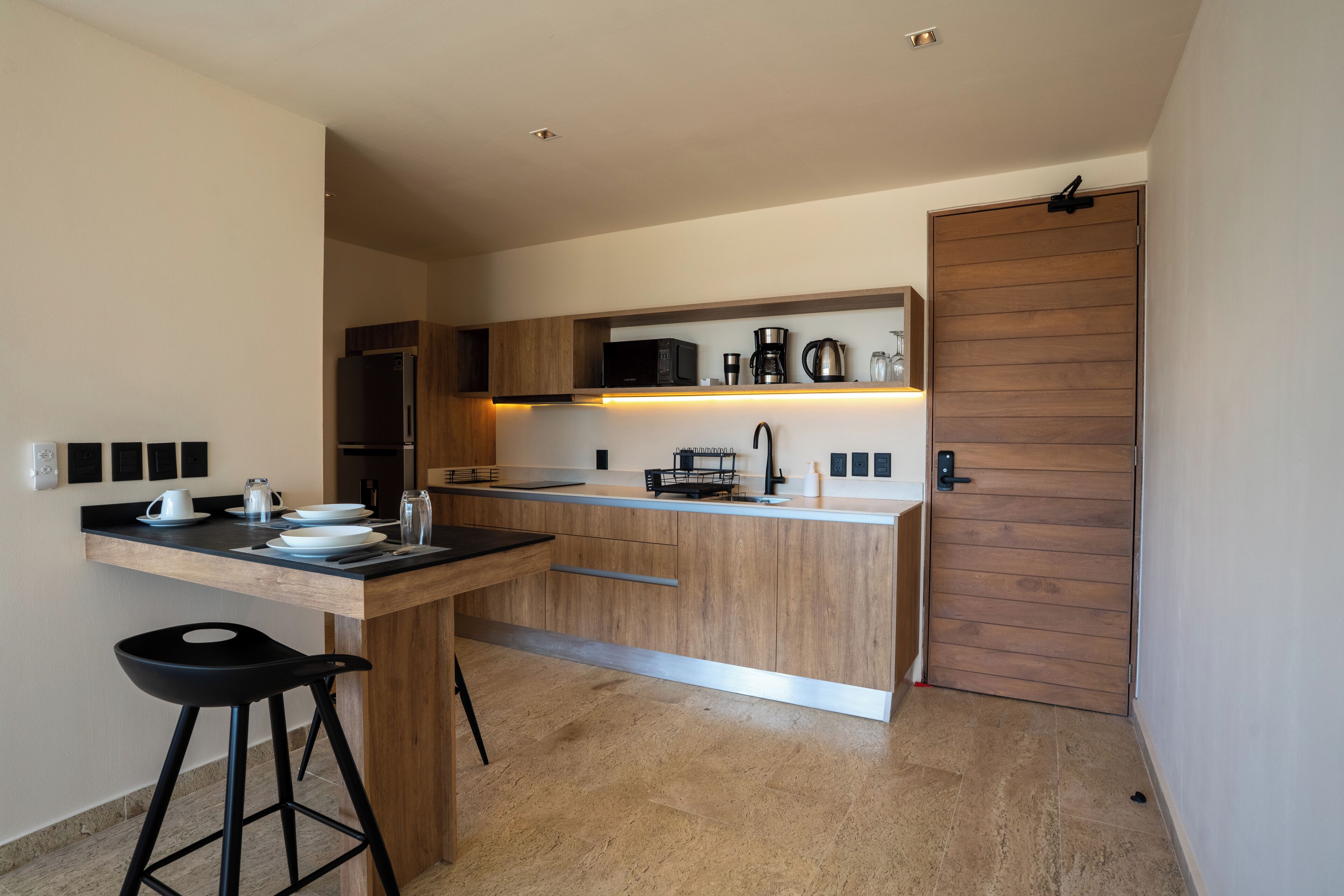 A modern kitchen with a wooden island, black bar stools, and a built-in microwave.