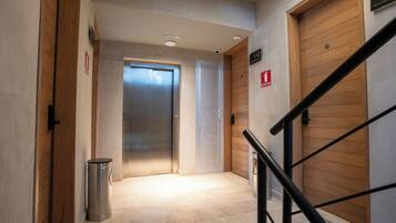A hallway with a trash bin, two doors, a staircase, and a fire exit sign.
