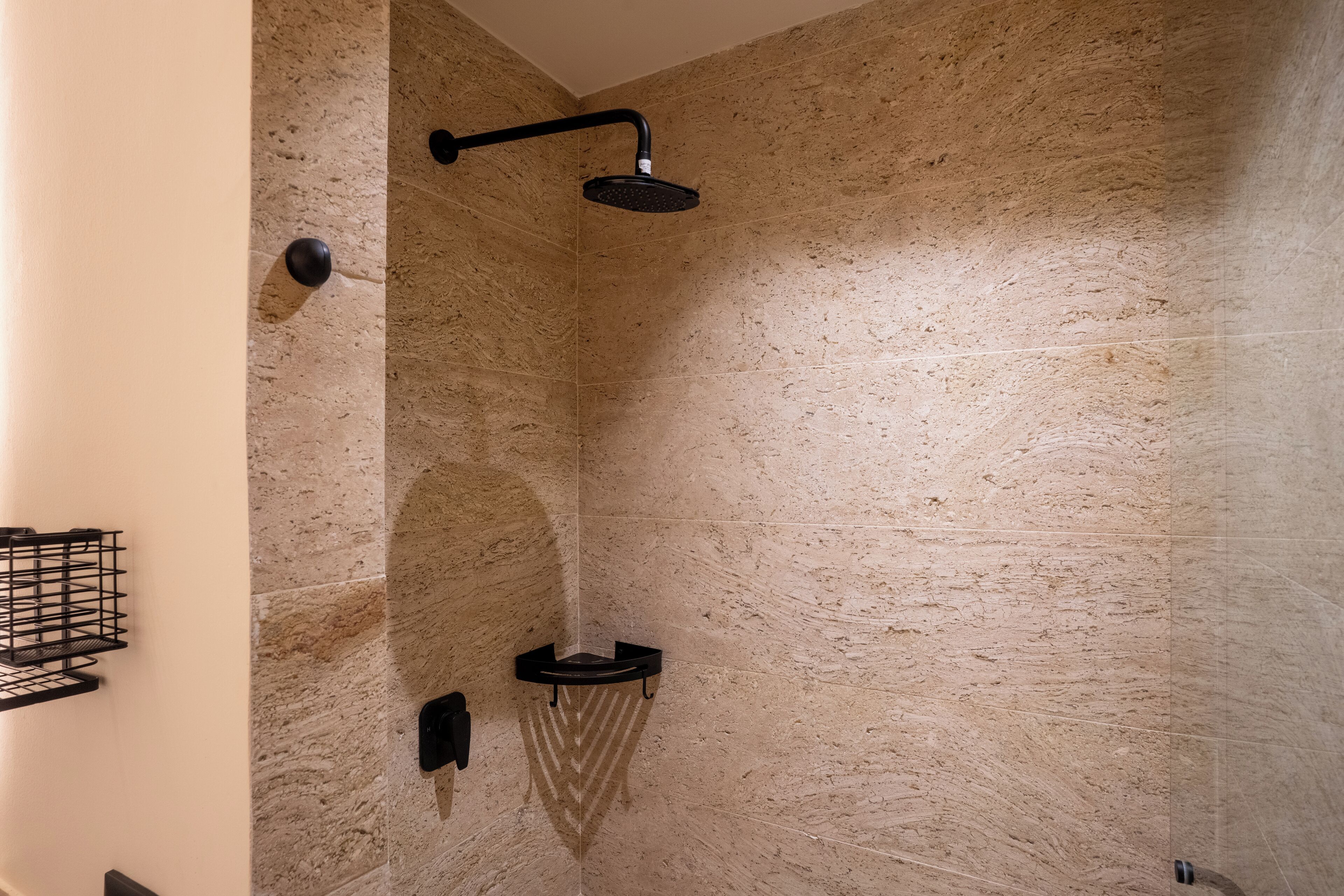 A modern bathroom with a stone wall, a black showerhead, and a black shelf.
