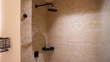 A modern bathroom with a stone wall, a black showerhead, and a black shelf.