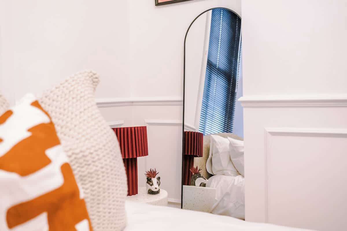 A bedroom with a bed, a large mirror, a red lamp, and a small decorative item on a nightstand.