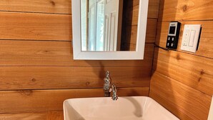 A bathroom with a white sink, wooden walls, a mirror, and a wooden countertop. - Tiny Tiger Shipping container with AC in charming Whitney (Whitney)
