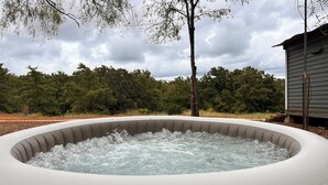A hot tub outdoors with a wooden structure in the background. - Tiny Tiger Shipping container with AC in charming Whitney (Whitney)