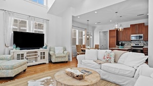 A spacious living room with a large flat-screen TV, a white sofa, a patterned armchair, and a wooden coffee table. - Serene 30A Getaway Steps From the Gulf With BBQ & Wraparound Porch 30A Fade Away by Avantstay (Santa Rosa Beach)