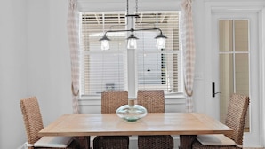 A dining room with a wooden table, woven chairs, a glass bowl centerpiece, and a black chandelier. - Serene 30A Getaway Steps From the Gulf With BBQ & Wraparound Porch 30A Fade Away by Avantstay (Santa Rosa Beach)