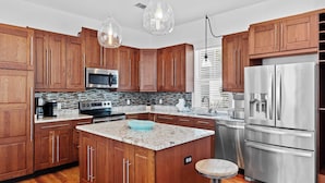 A modern kitchen with wooden cabinets, stainless steel appliances, a granite countertop, and pendant lighting. - Serene 30A Getaway Steps From the Gulf With BBQ & Wraparound Porch 30A Fade Away by Avantstay (Santa Rosa Beach)