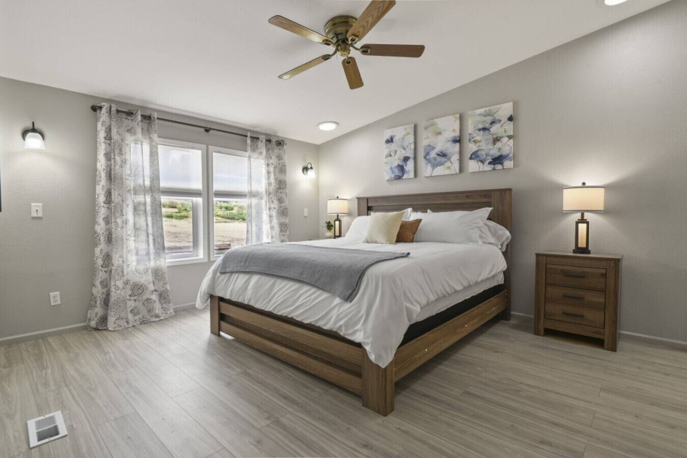 A bedroom with a wooden bed, a ceiling fan, a nightstand, and artwork on the wall.