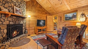 Un intérieur de chalet chaleureux avec une cheminée en pierre, des murs en bois, un téléviseur et un coin salon confortable.