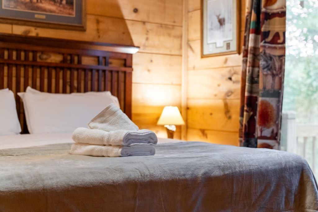 A neatly made bed with folded towels, a wooden headboard, and a lamp on a bedside table.