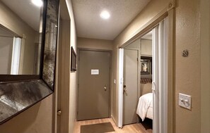 Un couloir avec une porte, un miroir et un lit dans la pièce adjacente.