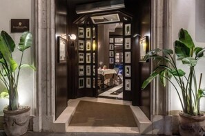 Een hotelentree met een receptiebalie, ingelijste foto's aan de muur en potplanten.